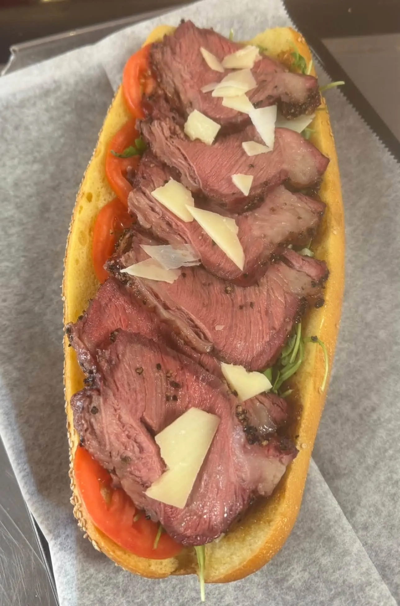 A generous roast beef sandwich topped with shaved cheese